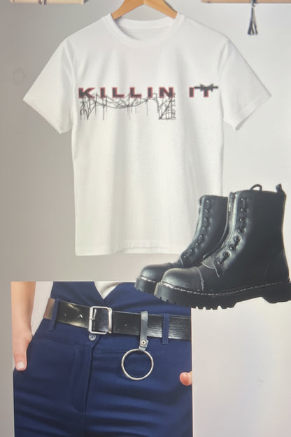 A white graphic T-shirt with 'KILLIN IT' text and a distressed design, shown hanging on a wooden hanger with a pair of black lace-up combat boots and dark blue pants below it.