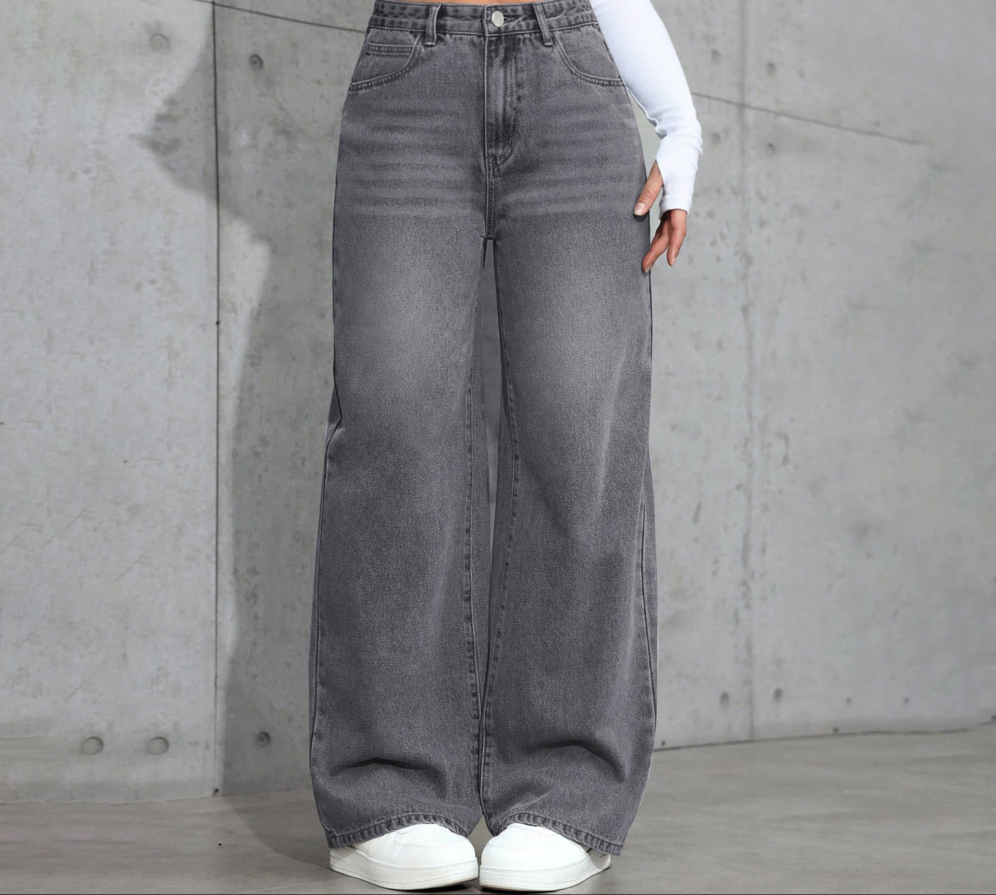 Person wearing gray wide-leg jeans against a concrete wall.