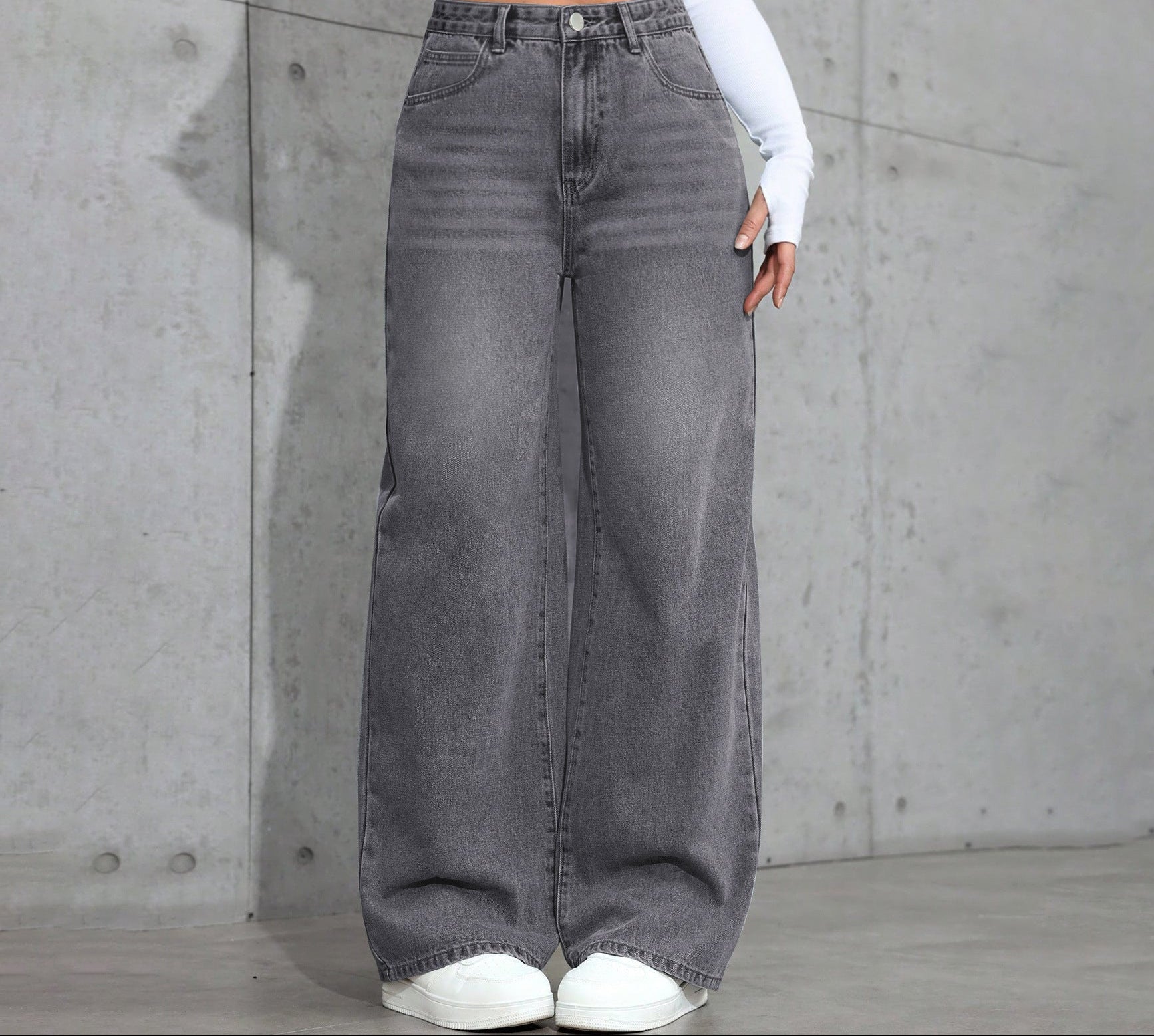 Person wearing gray wide-leg jeans against a concrete wall.