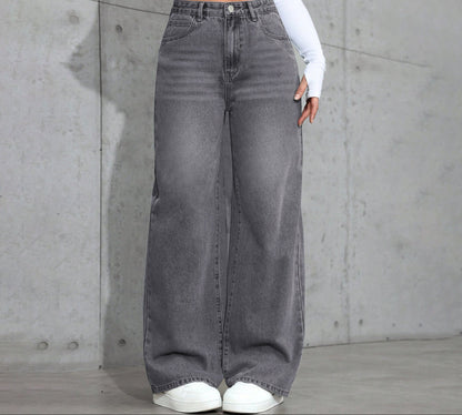 Person wearing gray wide-leg jeans against a concrete wall.