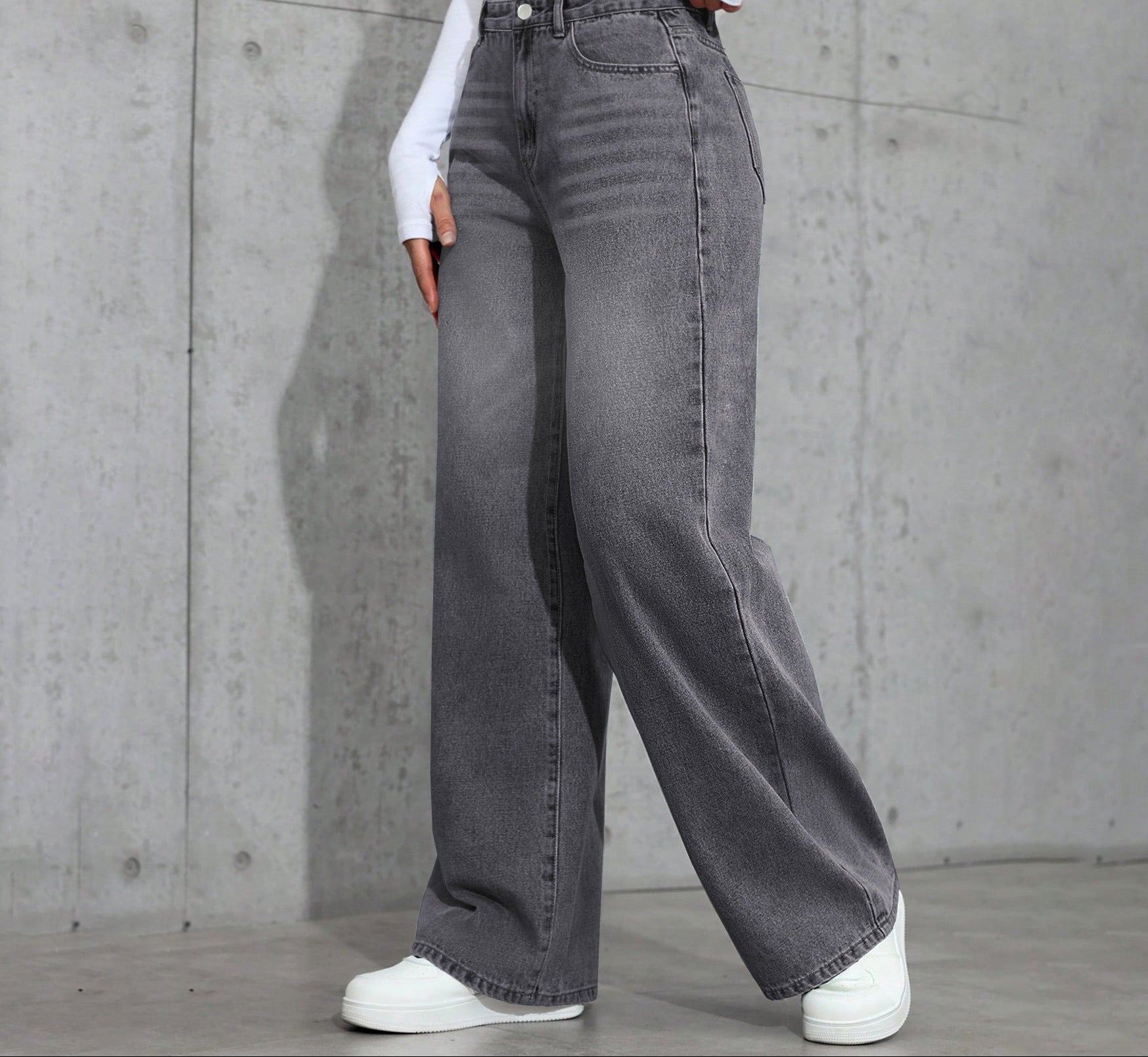 Person wearing gray wide-leg jeans and white sneakers against a concrete wall.