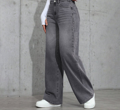Person wearing gray wide-leg jeans and white sneakers against a concrete wall.